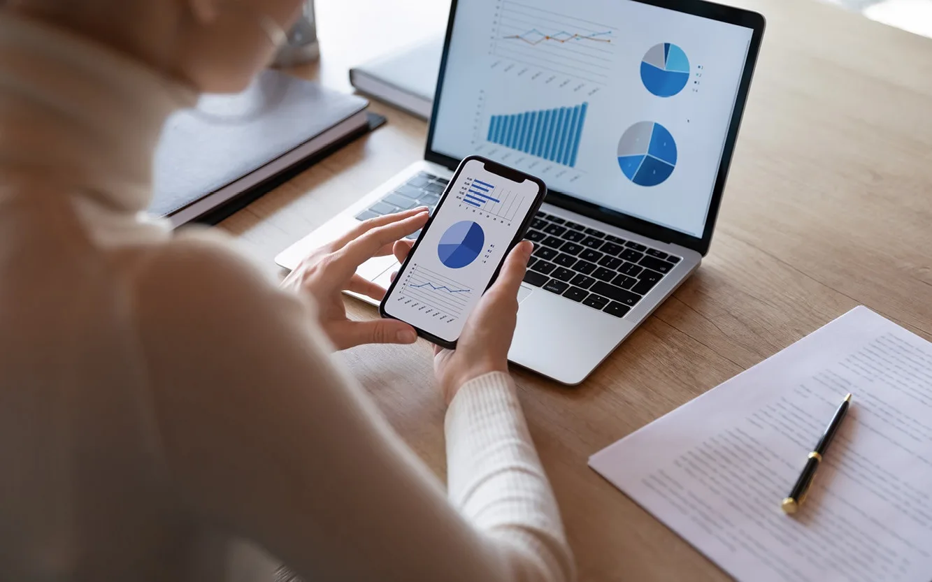 Person looking at graph on mobile and using laptop