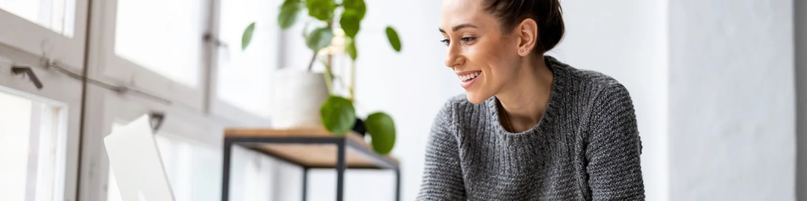 Happy woman sitting near window working on laptop