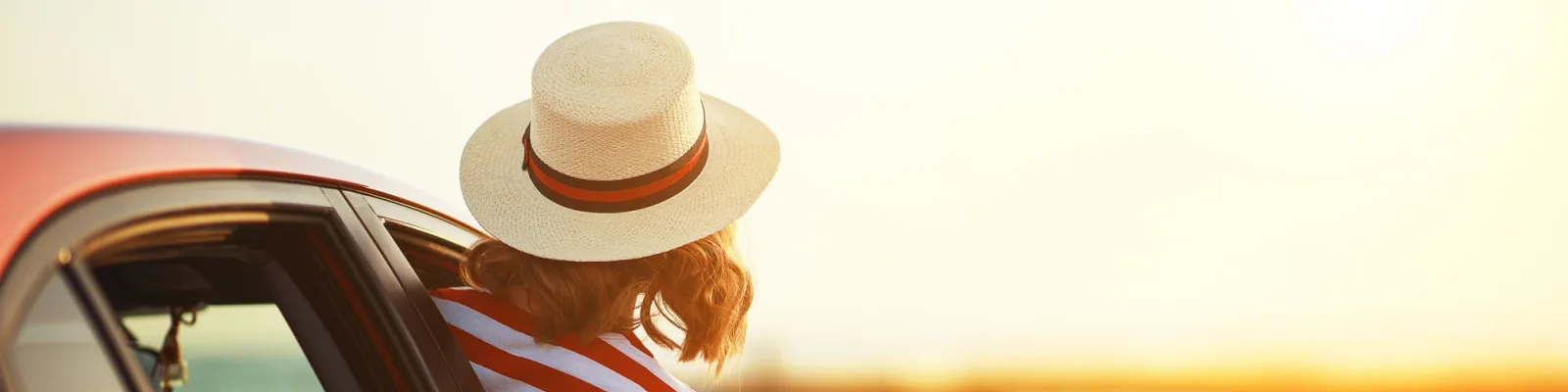 Young woman leaning outside car window on beach looking at sunset