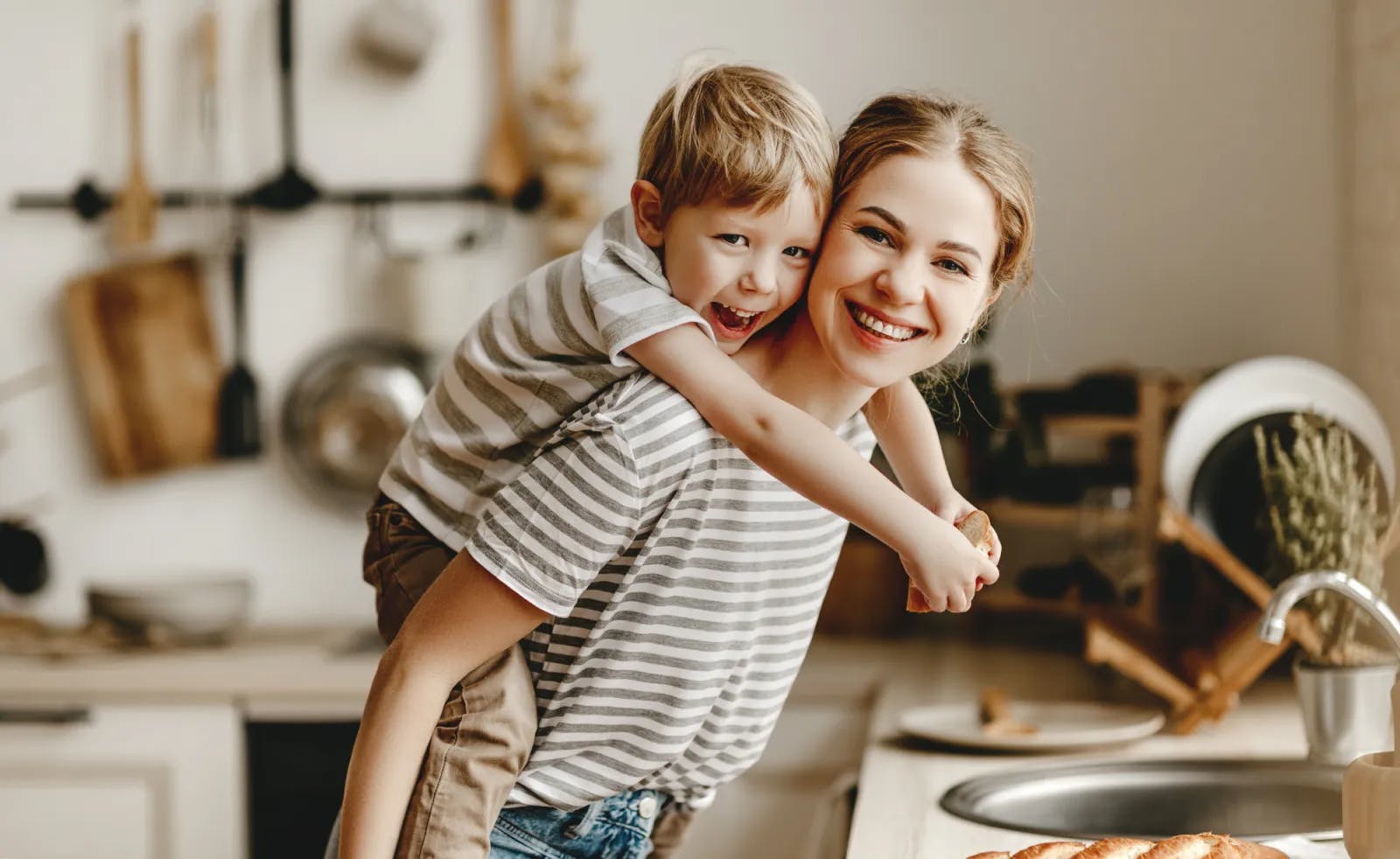 Mother giving son a piggy back ride in kitchen smiling