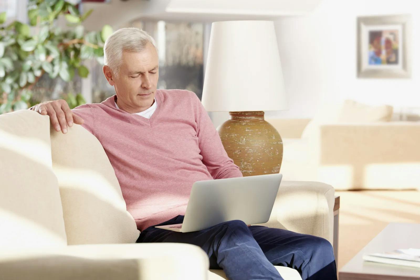 Senior man sitting on couch in living room looking at laptop