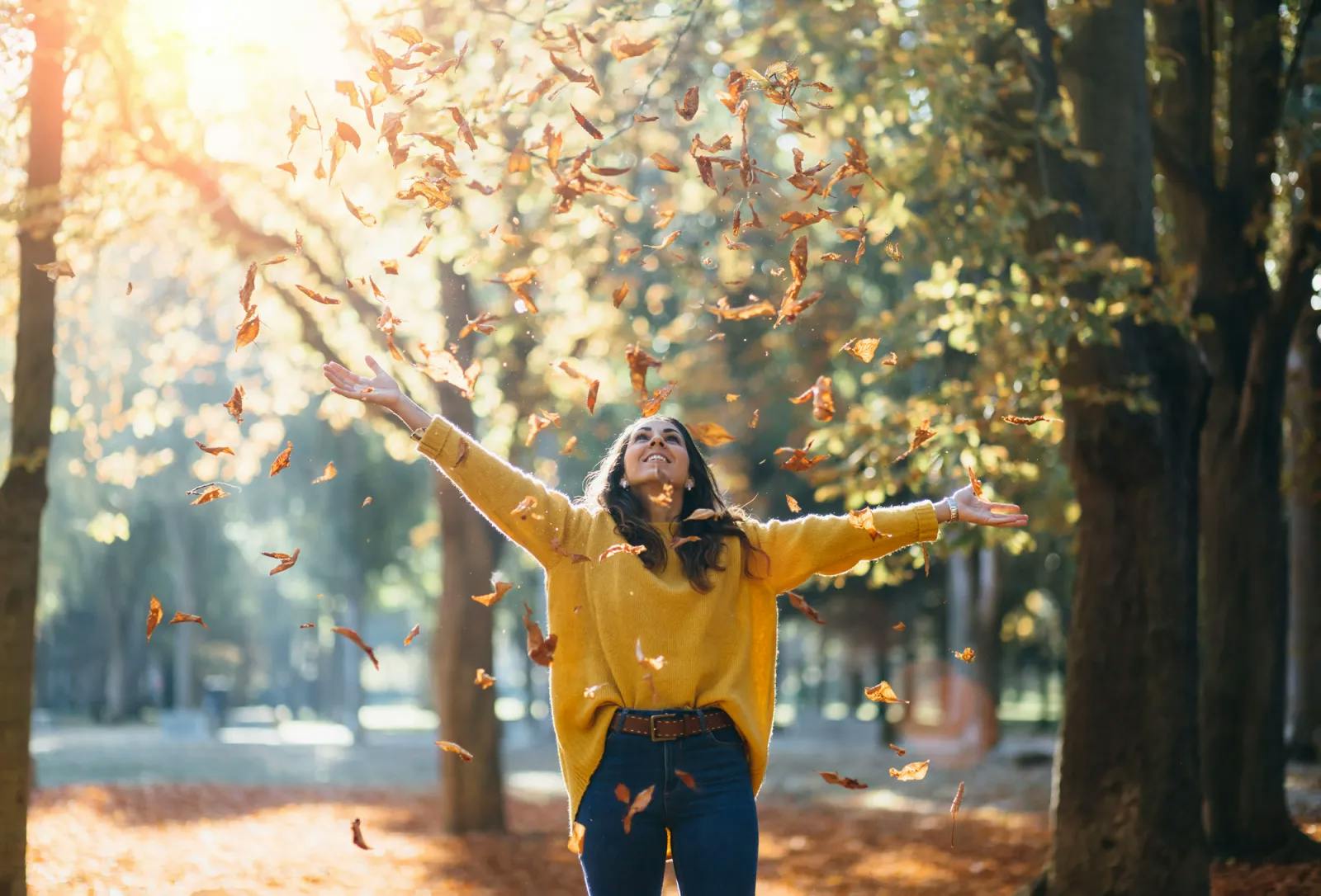 Young woman in yellow jumper playing outside with autumn leaves