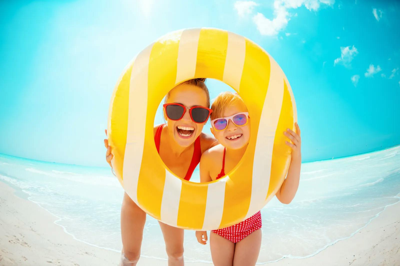 Mother and daughter smiling at the beach with sunglasses