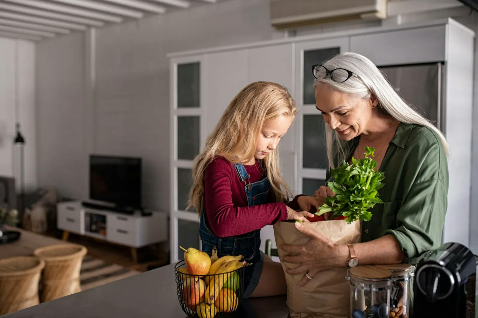 Grandmother and granddaughter unpacking groceries in the kitchen