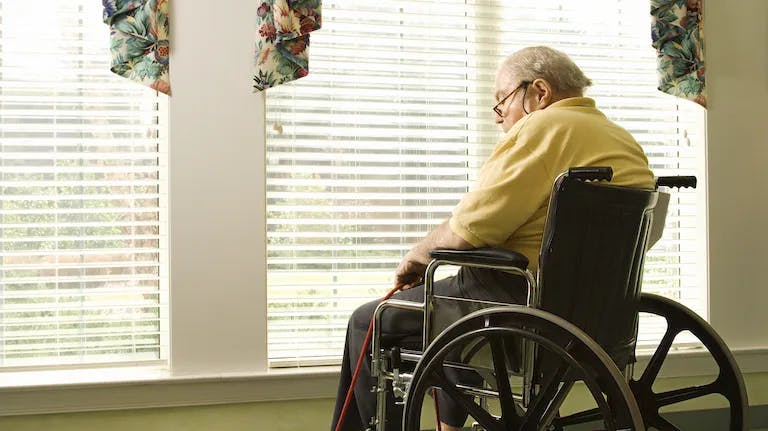 Senior man in wheelchair looking outside window in retirement home