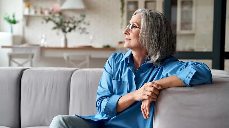 Senior woman sitting on couch looking outside window