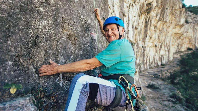 Smiling senior man rock climbing