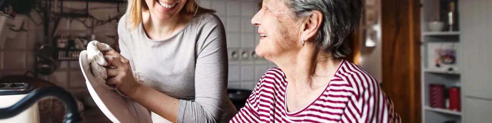 Adult daughter and elderly woman in kitchen smiling
